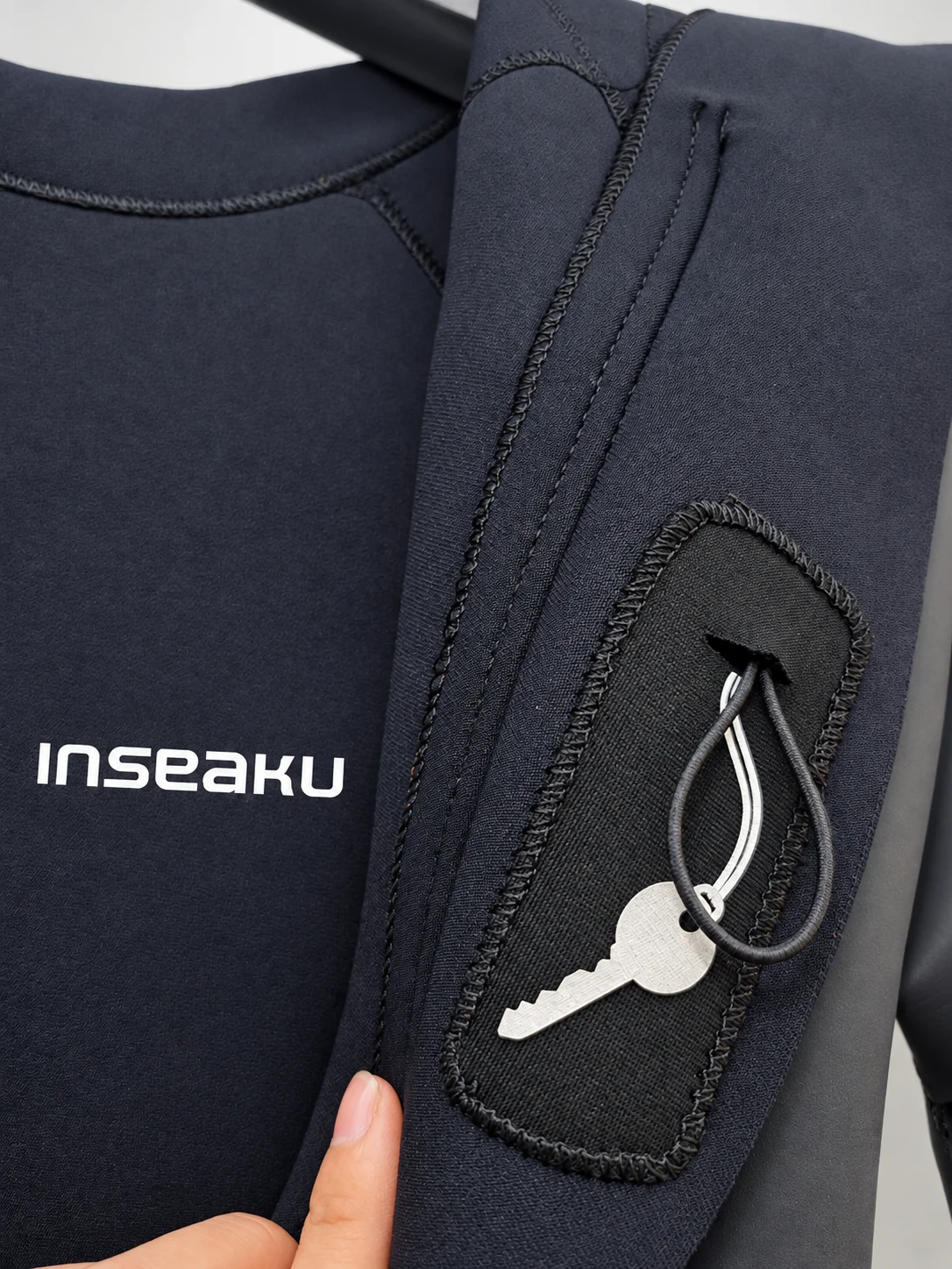 A small key secured to an inner loop near the rear zipper. Detail of the INSEAKU orange pattern sleeve triathlon wetsuit.