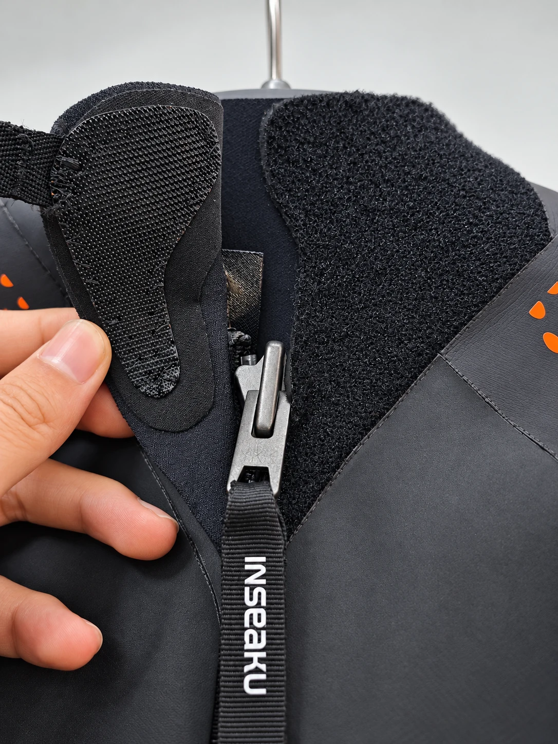 Rear zipper slider and folded neck closure flap. Detail of the INSEAKU orange pattern sleeve triathlon wetsuit.